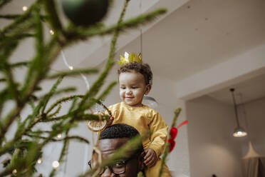 Vater mit Tochter berührt Weihnachtsschmuck zu Hause - MDOF00590