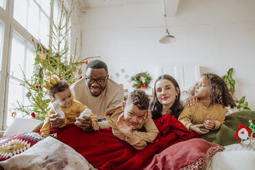 Glückliche Eltern mit Töchtern und Sohn, die sich zu Weihnachten im Wohnzimmer vergnügen - MDOF00593