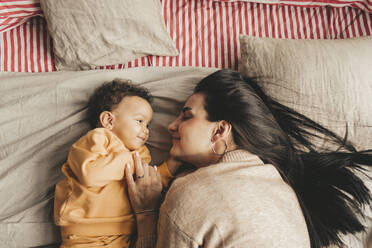 Smiling mother with cute daughter lying on bed at home - MDOF00594