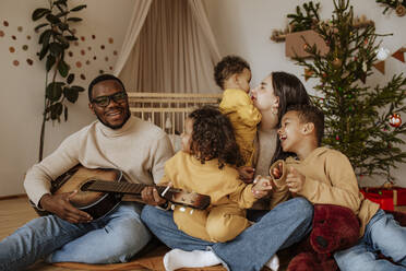 Cheerful family spending time together at Christmas playing the guitar - MDOF00602