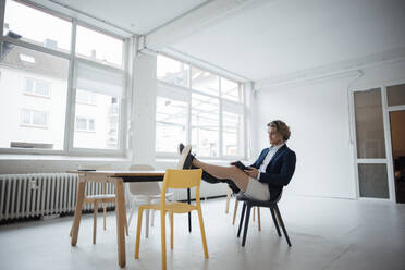 Junger Geschäftsmann mit Tablet-PC auf einem Stuhl im Büro sitzend - JOSEF16508