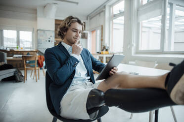 Businessman using tablet PC sitting on chair in office - JOSEF16509