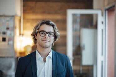 Smiling businessman wearing eyeglasses in office - JOSEF16512