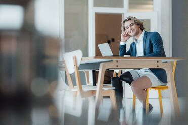 Glücklicher Geschäftsmann sitzt mit Laptop am Schreibtisch im Büro - JOSEF16545