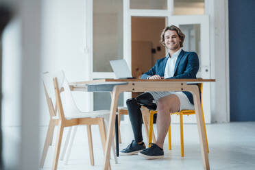 Lächelnder Geschäftsmann sitzt mit Laptop am Schreibtisch im Büro - JOSEF16546