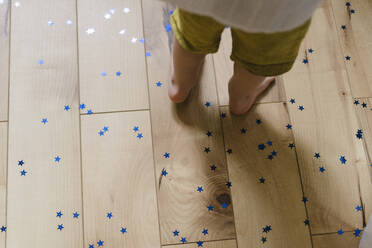 Junge steht auf Hartholzboden mit sternförmigem Konfetti - SEAF01742
