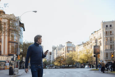 Mann mit Mobiltelefon beim Überqueren der Straße in der Stadt - JOSEF16612