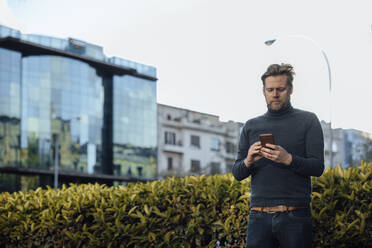 Man using mobile phone in front of plants - JOSEF16620