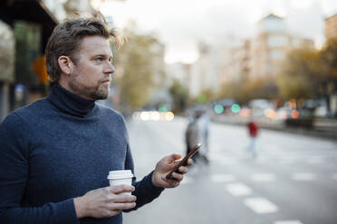 Man with mobile phone and disposable coffee cup on street - JOSEF16636