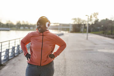 Smiling woman with wireless headphones exercising at promenade - JCCMF09288