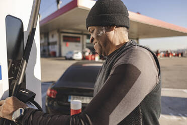 Ein älterer Mann lädt sein Elektroauto an einer Tankstelle auf - JCCMF09302