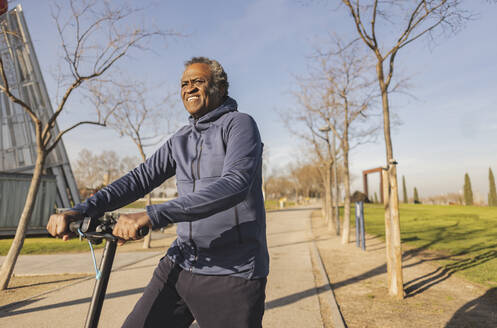 Thoughtful senior man riding electric push scooter on sunny day - JCCMF09311