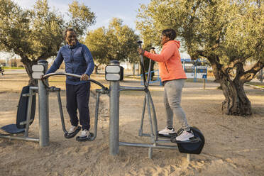 Happy senior couple exercising at outdoor equipment at park - JCCMF09332