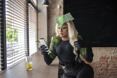 Blonde Drag-Queen benutzt Handy am Tisch im Cafe - VRAF00065