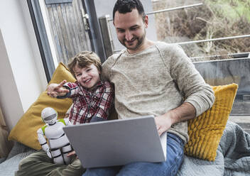 Happy son showing peace sign with father using laptop at home - UUF28066