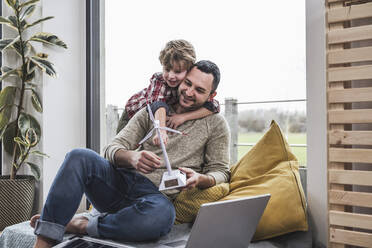 Son embracing father holding wind turbine model at home - UUF28072