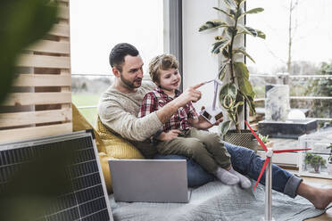 Vater berührt das Modell einer Windkraftanlage, während sein Sohn zu Hause sitzt - UUF28076