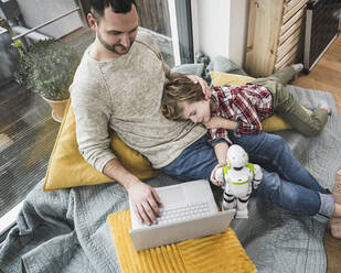 Son napping on father using laptop at home - UUF28095
