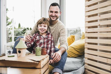 Lächelnder Vater und Sohn mit Modellhaus zu Hause - UUF28099