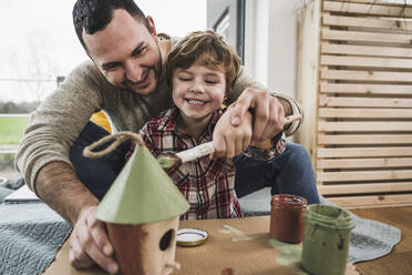 Happy father and son painting model house together at home - UUF28102