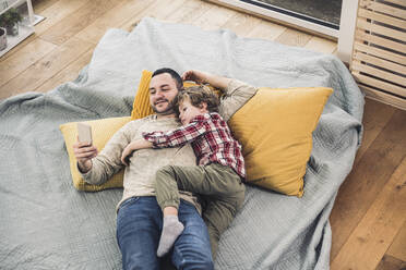 Glücklicher Vater, der ein Smartphone benutzt, während sein Sohn zu Hause auf einer Decke liegt - UUF28112