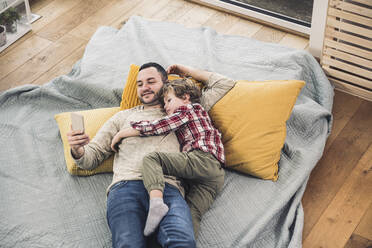 Happy father using smart phone with son lying on blanket at home - UUF28112