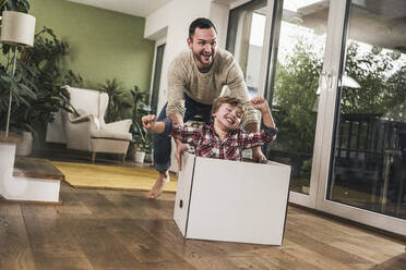 Glücklicher Junge, der mit seinem Vater Spaß hat, wenn er zu Hause einen Karton schiebt - UUF28126