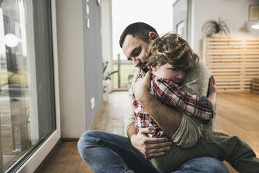 Father and son hugging each other on floor at home - UUF28133