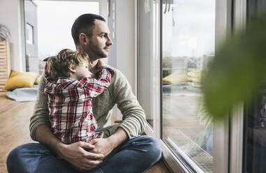 Father and son sitting by glass door at home - UUF28134