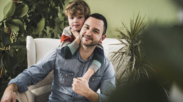 Smiling father with son sitting on armchair at home - UUF28139