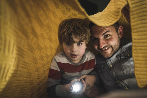 Glücklicher Vater mit Sohn, der eine Fackel unter einer gelben Decke hält - UUF28147