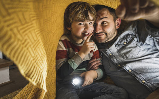 Lächelnder Vater mit Sohn, der unter einer gelben Decke gestikuliert und eine Fackel hält - UUF28149
