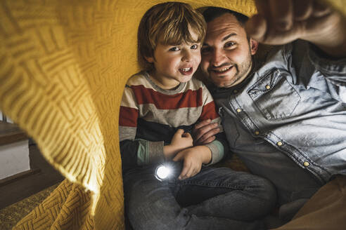 Lächelnder Vater mit Sohn, der eine Fackel unter einer gelben Decke hält - UUF28150