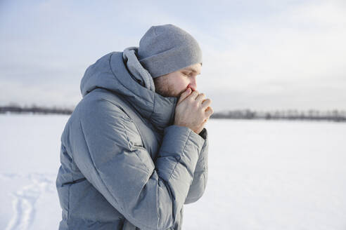 Mann mit Strickmütze wärmt Hände im Winter - EYAF02556