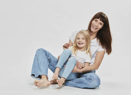 Glückliche Tochter sitzt mit Mutter gegen weißen Hintergrund - DHEF00680
