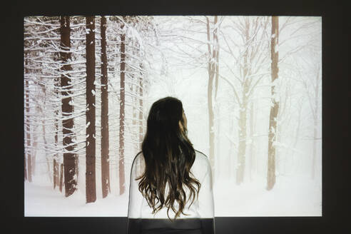 Woman looking at snowy forest projection on wall - MRAF00918