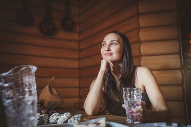 Lächelnde Frau mit Trinkglas, die in der Sauna nachdenkt - MDOF00606