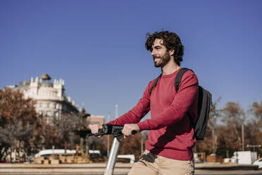 Happy man with electric push scooter standing on sunny day - EBBF07829