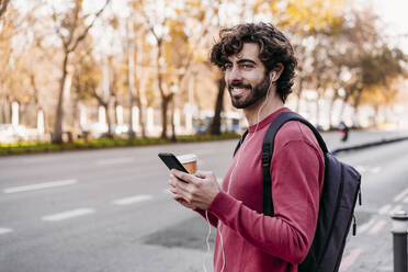 Lächelnder Mann mit Smartphone auf dem Bürgersteig - EBBF07866