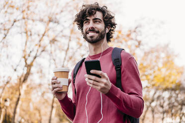 Lächelnder Mann mit Mobiltelefon und Kaffeetasse auf dem Fußweg - EBBF07868