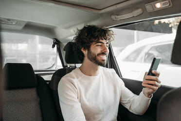 Glücklicher Mann mit Smartphone im Auto sitzend - EBBF07880