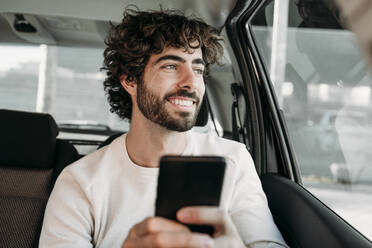 Smiling young man with smart phone sitting in car - EBBF07881