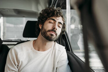 Young man with eyes closed leaning on car window - EBBF07883