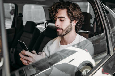 Young man using mobile phone traveling in car - EBBF07885