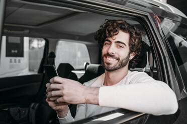Lächelnder Mann mit Smartphone auf Reisen im Auto - EBBF07887
