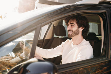 Happy young man with beard driving car on sunny day - EBBF07892