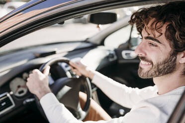 Lächelnder junger Mann mit Bart im Auto sitzend - EBBF07894