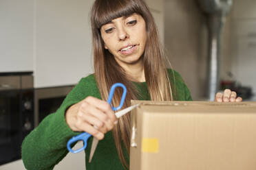 Mature woman unboxing package with scissors at home - VEGF06188