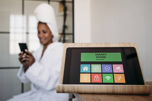 Hausautomatisierungs-App auf einem Tablet-PC mit einer Frau, die im Hintergrund ein Smartphone benutzt - EBBF07897