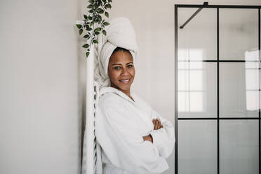 Smiling mature woman standing with arms crossed in bathroom at home - EBBF07900